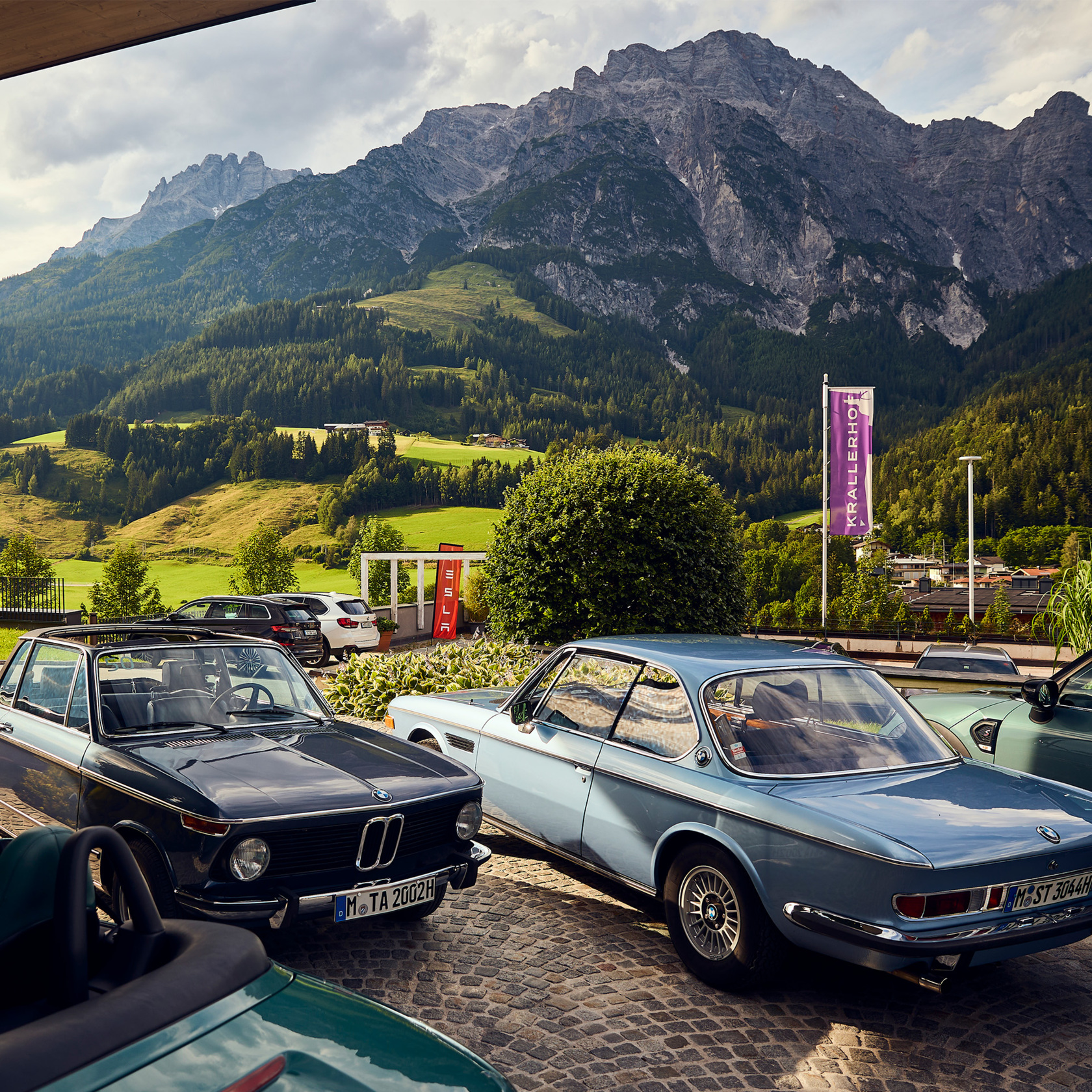 zwei BMW Oldtimer in schwarz und babyblau stehen geparkt vor einer Bergkulisse