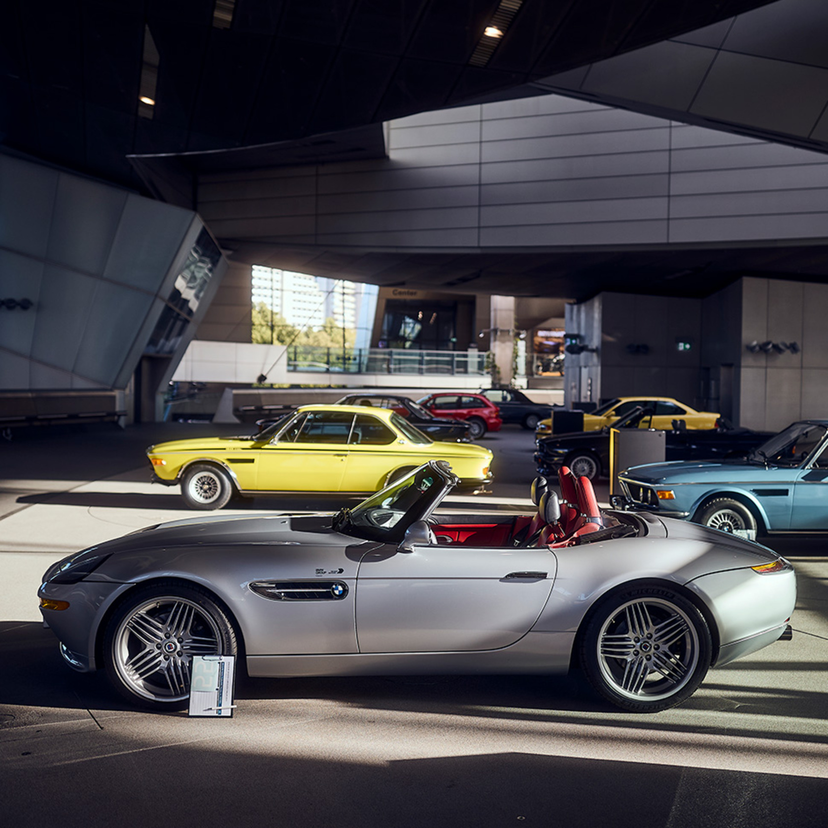 ein Blick in die BMW Welt zeigt ein silbernes BMW Cabrio und dahinter einen gelben BMW Oldtimer