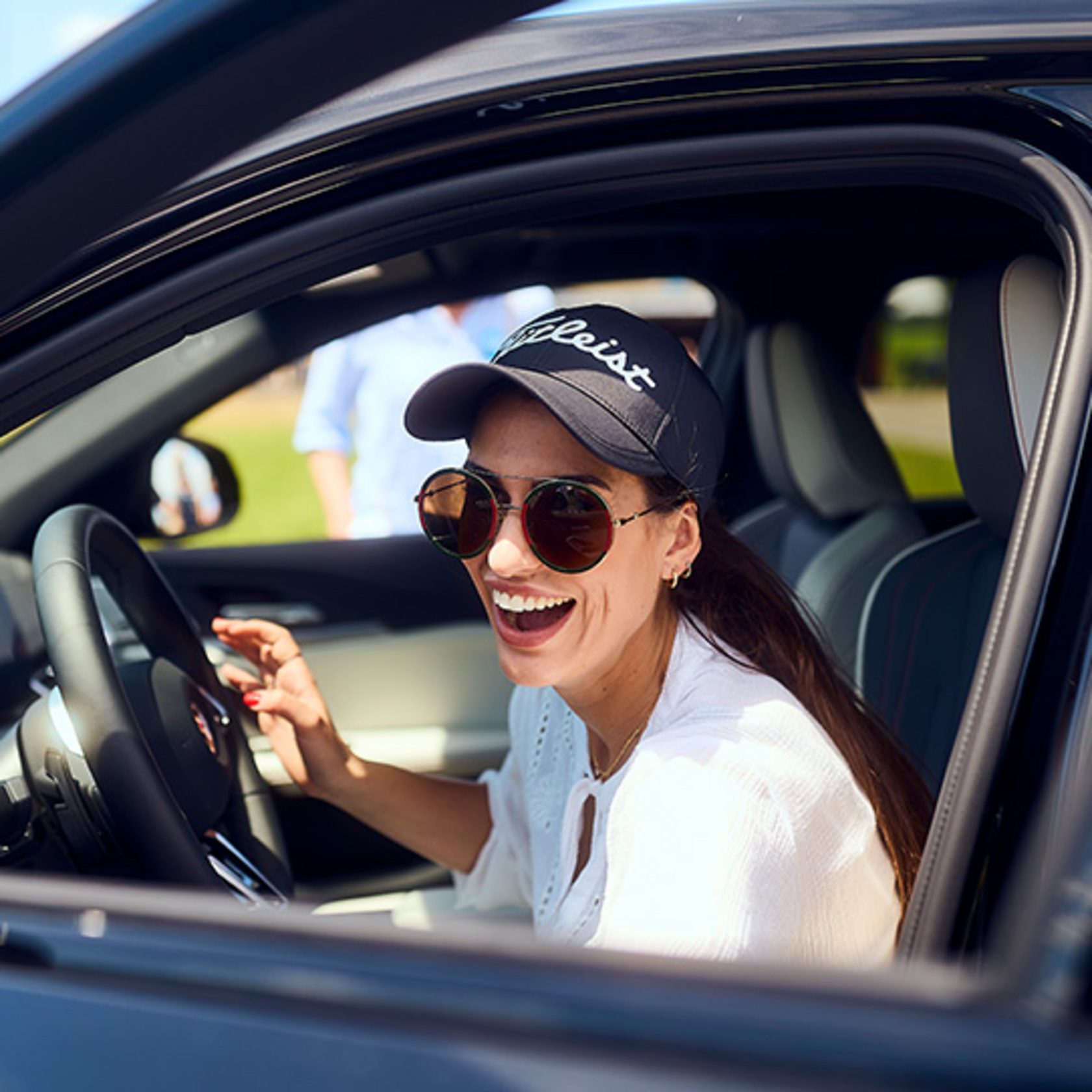 eine Frau mit Sonnenbrille und schwarzer Schirmmütze steigt lachend aus einem BMW aus