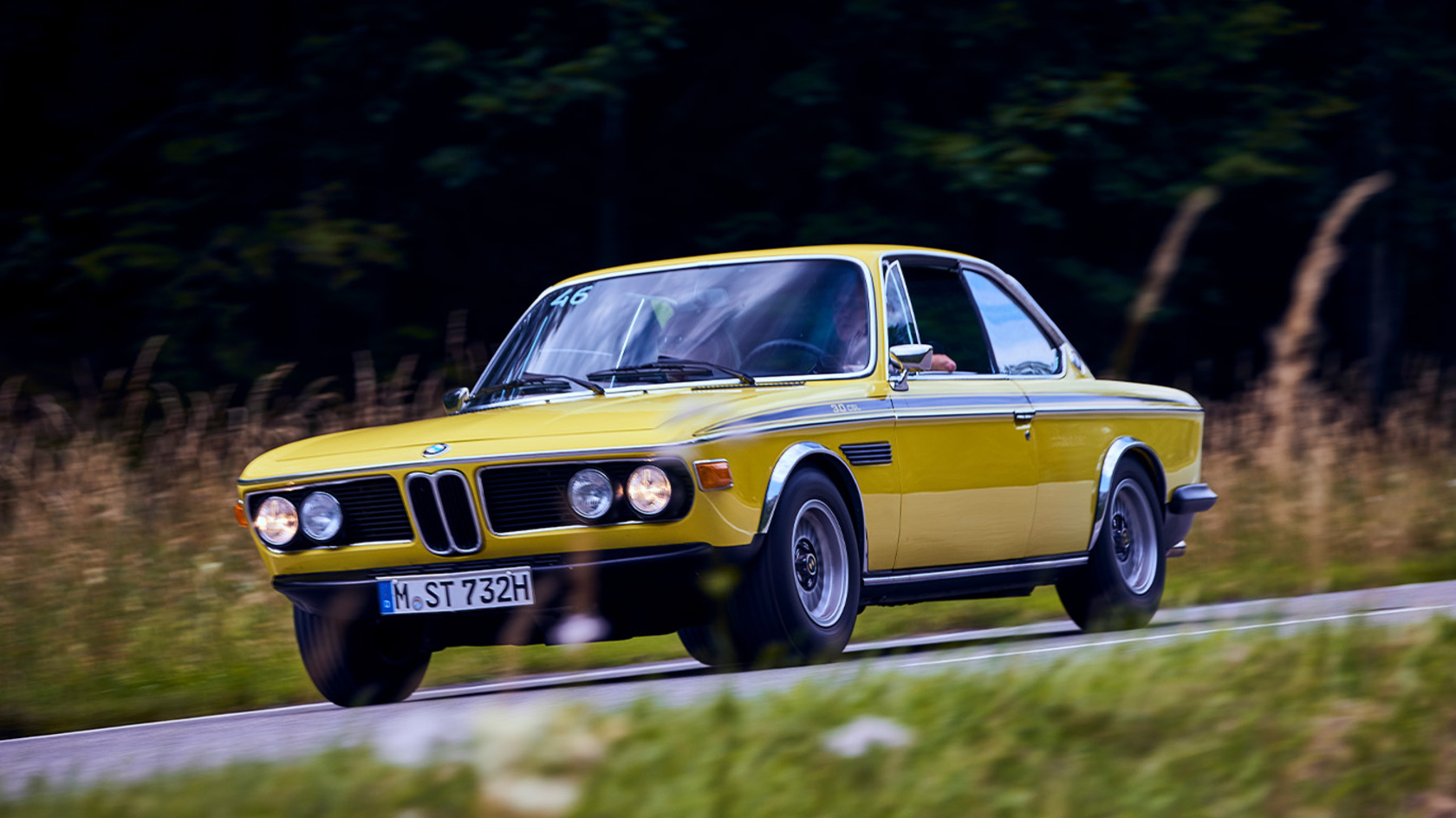 ein gelber BMW Oldtimer fährt eine Landstraße entlang