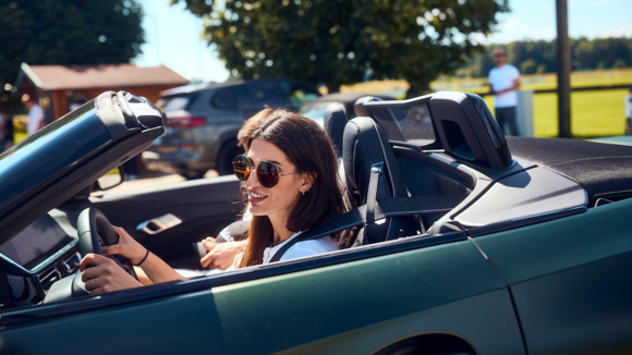 eine Frau mit braunen Haaren und Sonnenbrille sitzt in einem türkisfarbenen BMW Cabrio mit offenem Verdeck