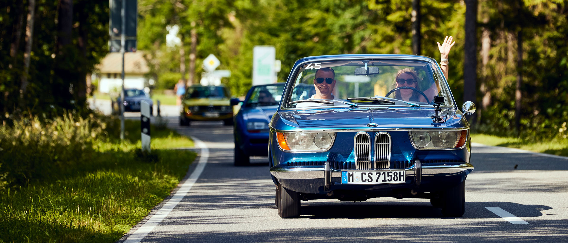 Ein blauer BMW Oldtimer fährt im Sonnenschein auf der Landstraße