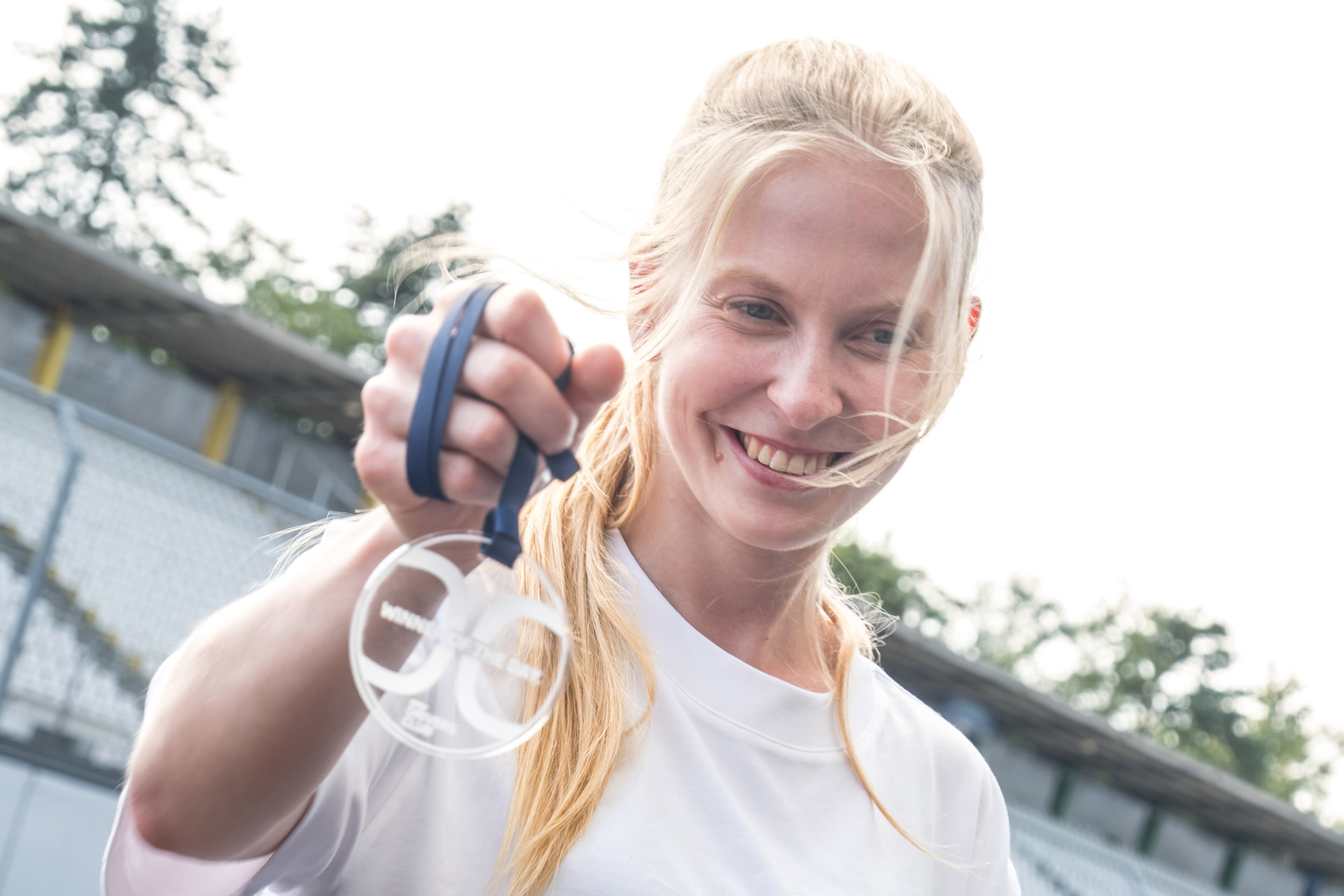 Eine blonde Frau hält lächelnd eine Drivers Club Medaille ins Bild