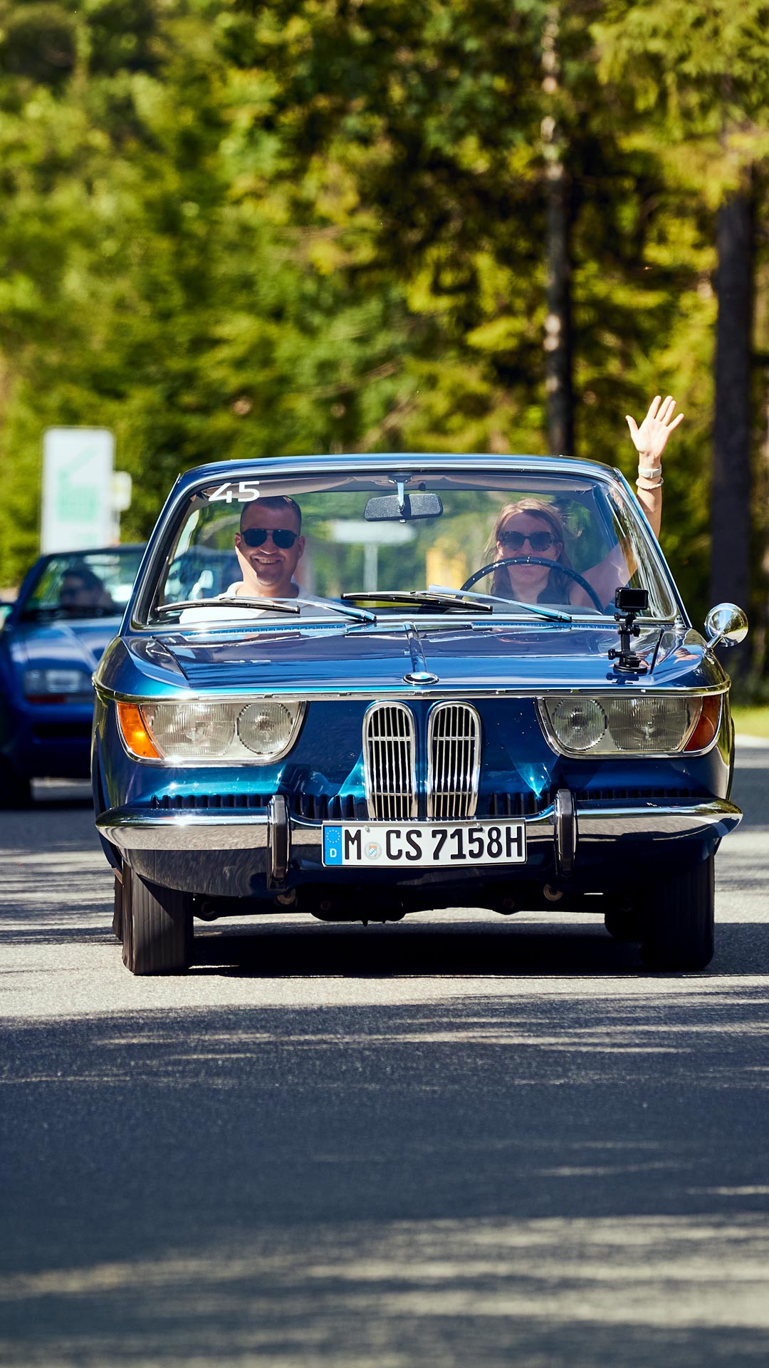 Ein blauer BMW Oldtimer fährt im Sonnenschein auf der Landstraße