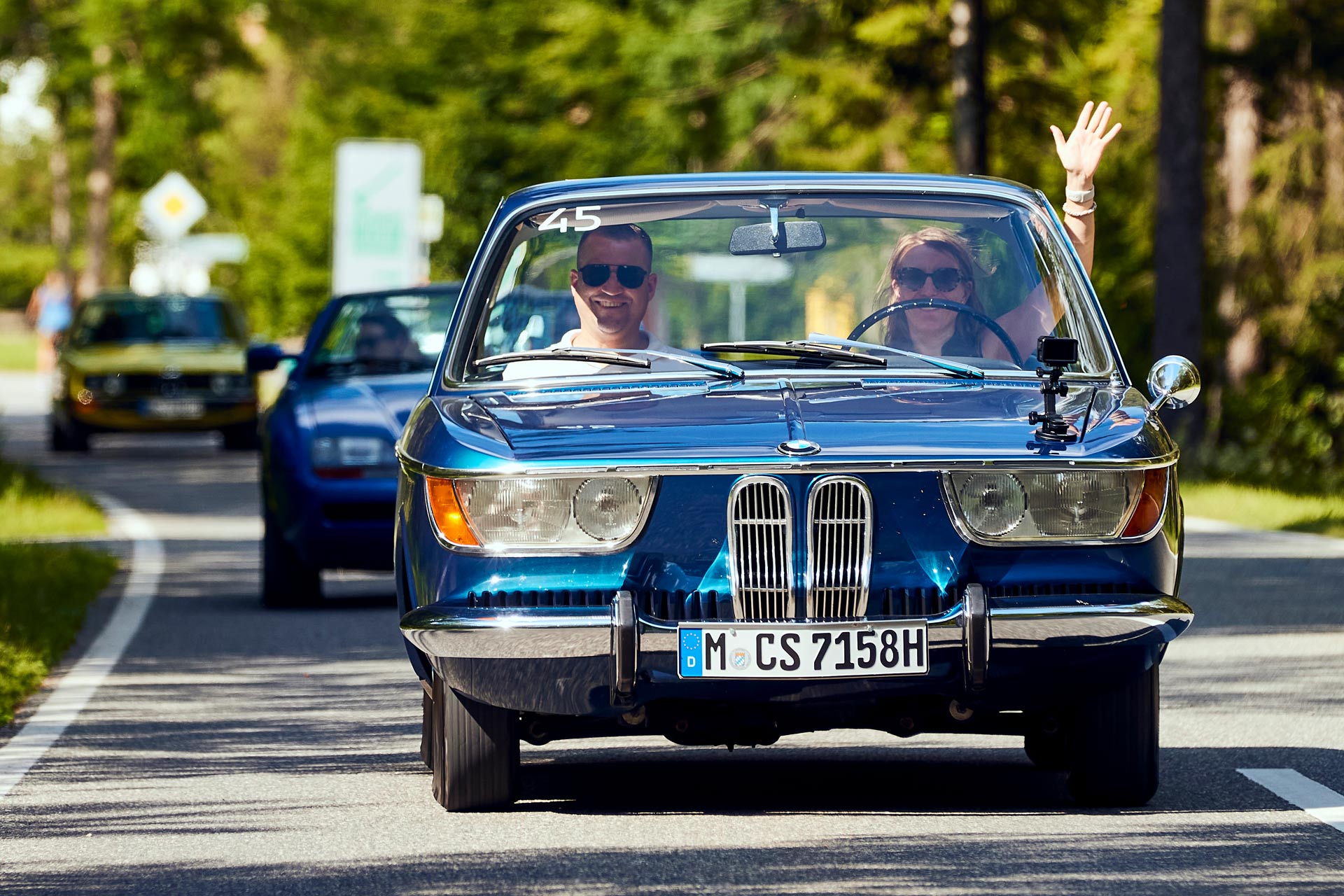 Ein blauer BMW Oldtimer fährt im Sonnenschein auf der Landstraße
