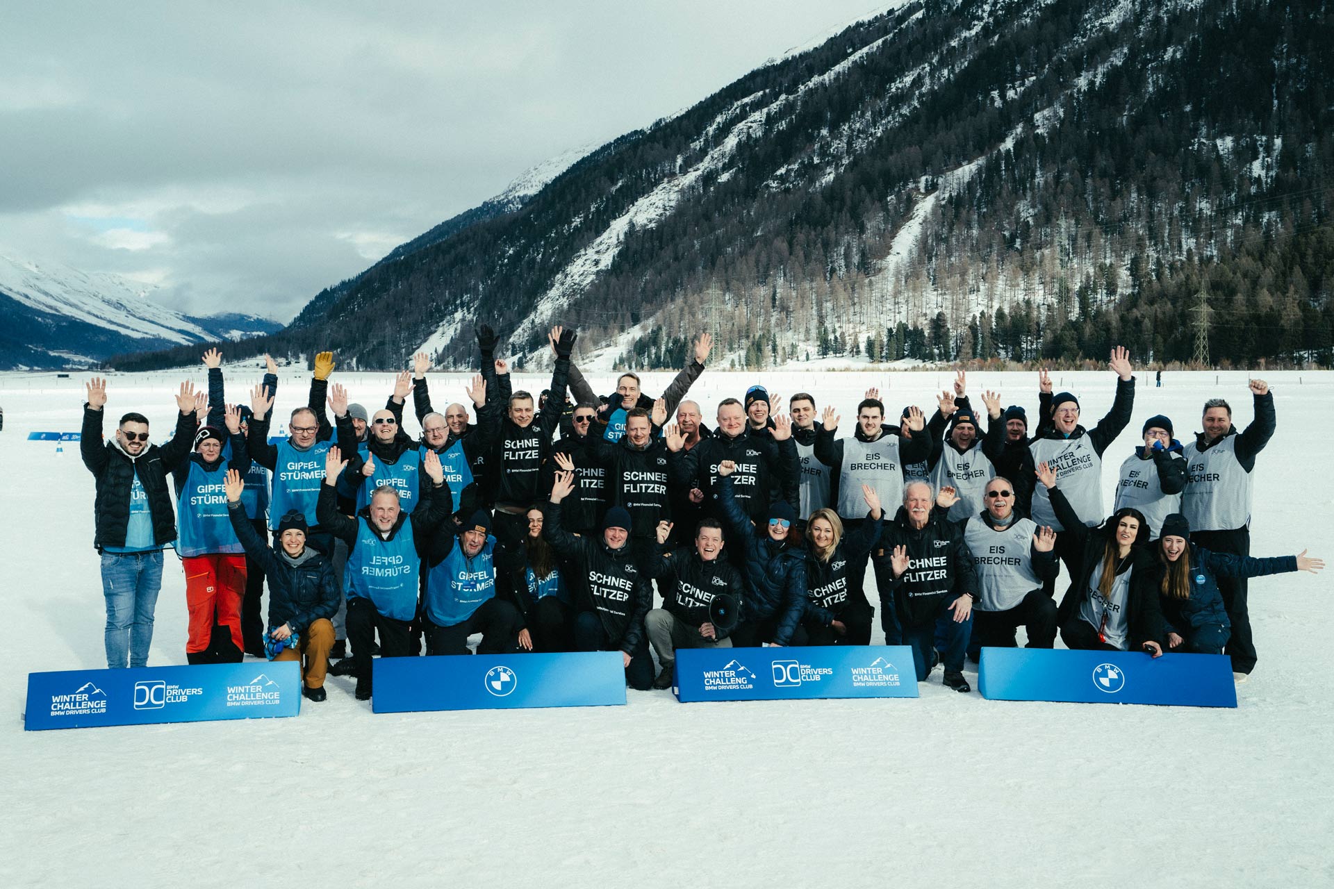 das Team und die Teilnehmer der Winter Challenge stehen im Schnee auf einem zugefrorenen See und jubeln